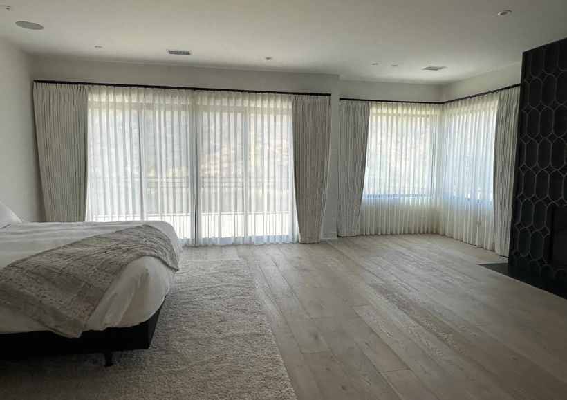 Floor-to-ceiling sheers and side panels across a bedroom wall of glass
