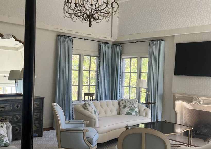 Powder-blue pinch-pleat drapery with trim at a traditional living room