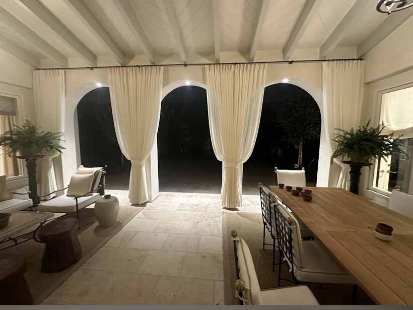 Cream pinch-pleat panels tied at arched openings on a covered terrace