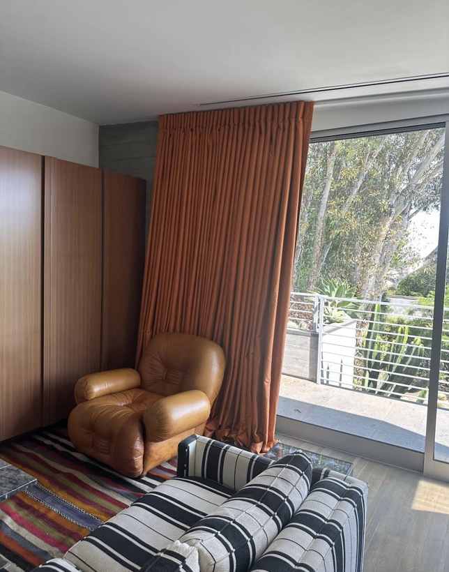 Rust pinch-pleat panel beside a leather lounge chair and glass wall